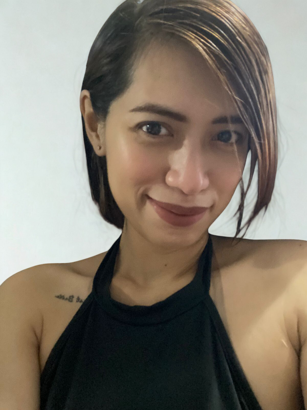 Smiling woman with short hair wearing a black halter top, facing the camera against a neutral background.