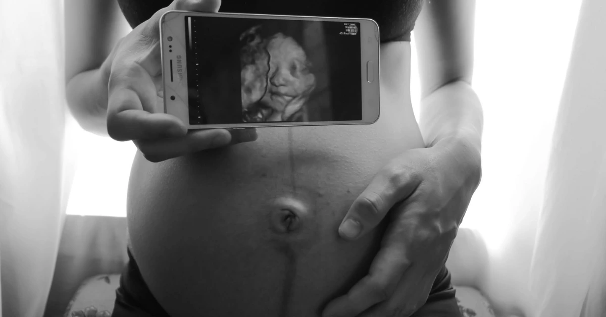 First time mom holding phone with ultrasound image over pregnant belly.