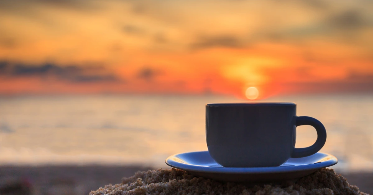 A cup of cold coffee on the beach at sunrise symbolizing the quiet moments in motherhood.