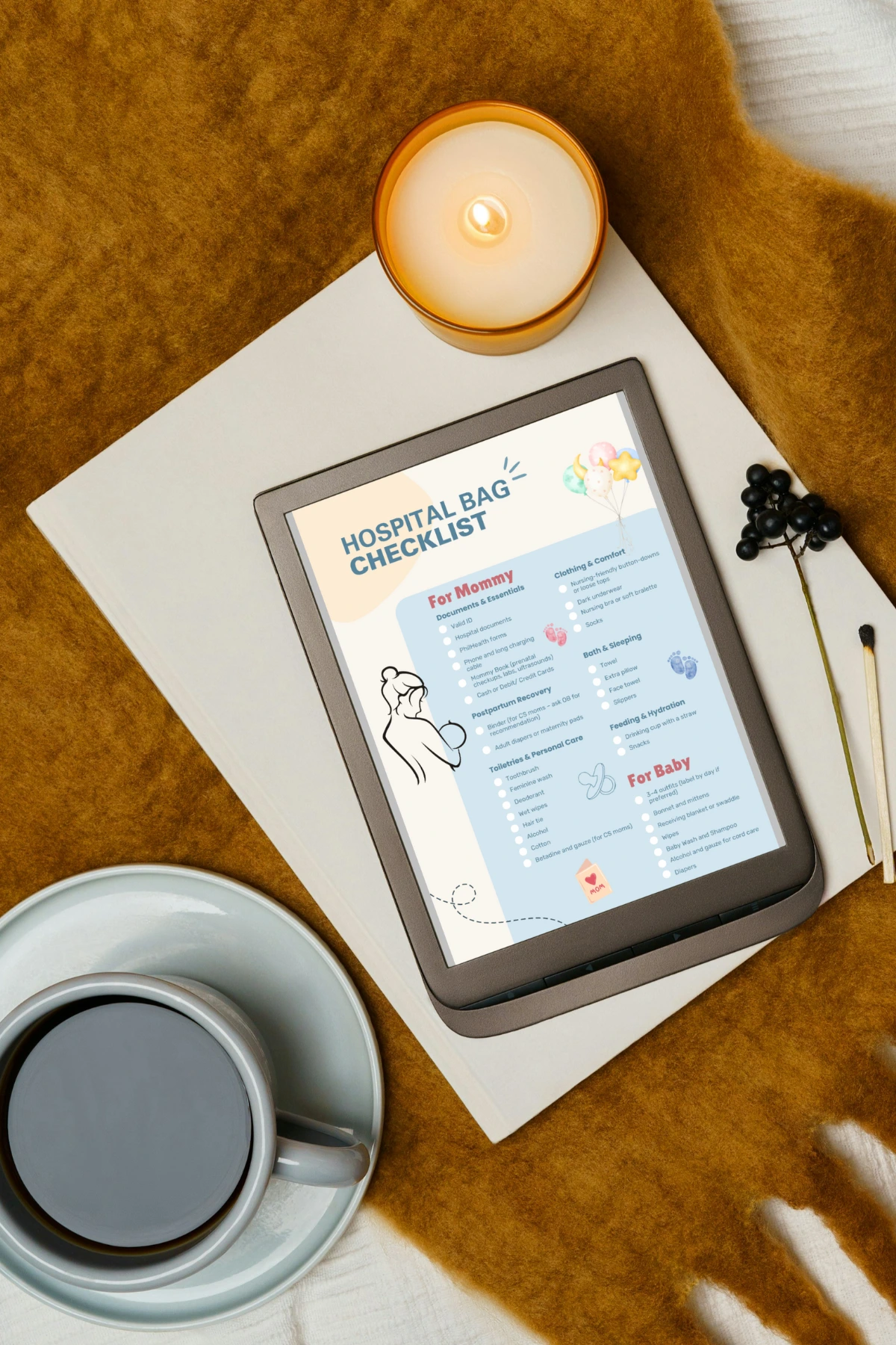 Flat lay of a digital hospital bag checklist on a tablet beside a candle, coffee cup, and brown blanket.