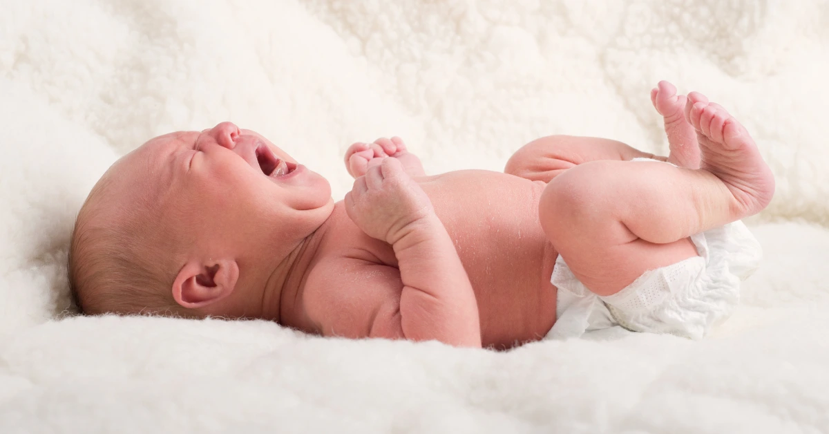 Newborn baby reacting with arms raised during Moro reflex.