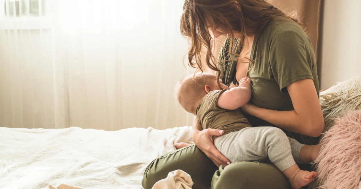 Mother breastfeeding baby on bed during her breastfeeding journey at home.
