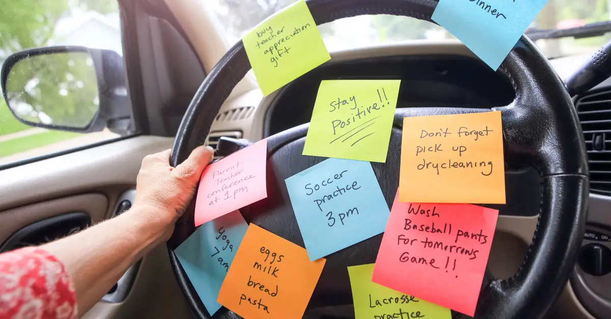 Steering wheel covered with colorful sticky notes reminding about errands, soccer practice, and groceries, symbolizing mom brain and mental load.