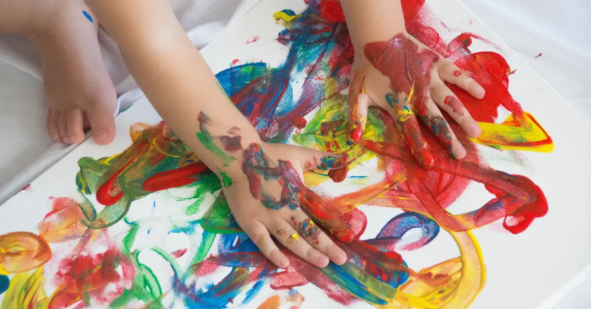 Toddler hands finger painting with bright colors as a fun indoor activity at home.